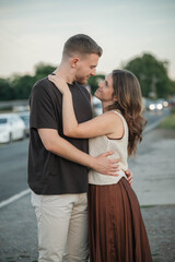 Loving couple embraces on the roadside, gazing into each other's eyes with affection, enjoying a romantic moment outdoors at sunset
