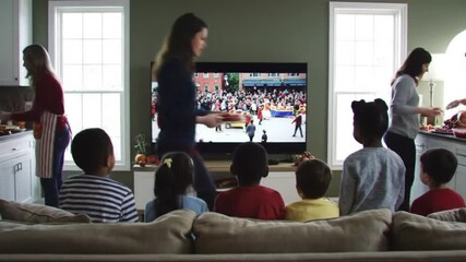 Family gathering in a cozy living room watching a colorful parade on TV while cooking