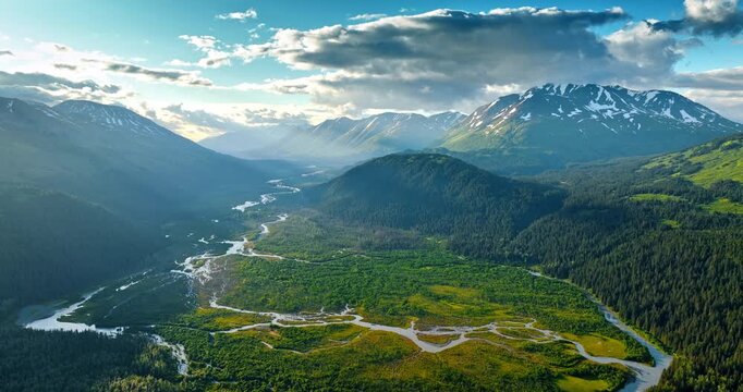 Approaching the spectacular valley crossed by the wavy river among the gorgeous mountains. Huge grey cloudscape hanging in the sky over the scenery. Alaska, USA.