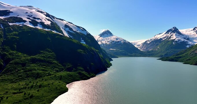 Footage over the lake sparkling in the sun among the verdant mountains. Beautiful snow-capped rocks in the scenery of Alaska, USA.