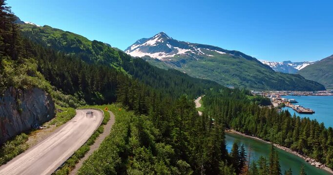 Following a car riding by the dangerous mountain road. Drone footage over the pine tree woods covering the spectacular rocks in Alaska, USA.