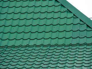 Green metal tiles cover the sloping roof of the house. Texture of roofing iron.