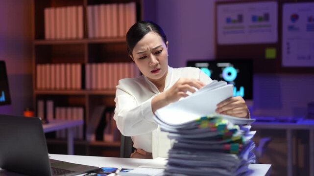 Exhausted businesswoman frantically searching through stacks of paperwork at dark office, experiencing overwhelming work stress and deadline pressure during late night shift
