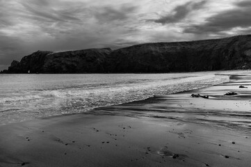 A black and white photo of a beach with a rocky cliff in the background