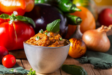 Eggplant caviar in a glass jar and vegetables on a wooden background.