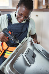 Technician repairing dishwasher using electric screwdriver in a kitchen