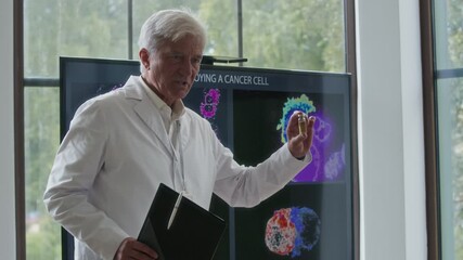 Senior oncologist holding injection vial with liquid medication speaking about targeted therapy for cancer during medical conference