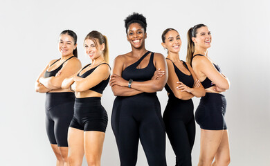 A group of five women in their 20s and 30s of different ethnicities and builds pose against a white background wearing black sportswear. They look happily at the camera with their arms crossed.