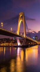 Fototapeta premium Modern cable-stayed bridge at twilight over a river. City lights reflect on water
