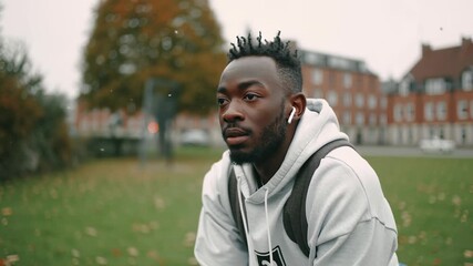Young handsome african man listening to music with wireless earphones in a park. Thoughtful student relaxing outdoors with a pensive expression - Powered by Adobe