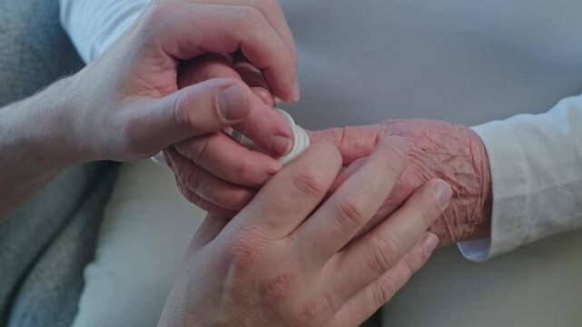 Close up of a woman's hands with tremor and a bottle of pills, a man helping her get pills