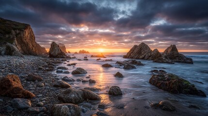 Dramatic sunset over a rugged, rocky coastline with waves crashing against sea stacks under a cloudy sky.
