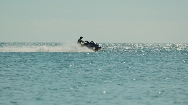 A person riding a jet ski swiftly glides across the clear blue ocean waters, leaving a spray of white foam in its wake, with a serene sky in the background