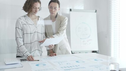 Two businesswomen analyzing financial reports and discussing growth strategies while collaborating in a modern office setting. Business people concept - Powered by Adobe