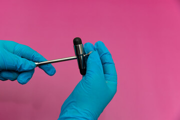 Blue Gloved Hands Holding medical hammer and medical needle On pink Background,