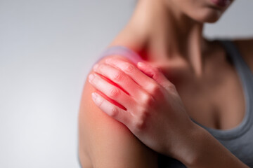 Woman experiencing shoulder pain and discomfort holding her inflamed joint with a red highlight indicating injury or strain in a health and wellness concept