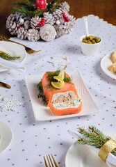 A cold appetizer, a terrine of salted salmon and smoked mackerel with cheese cream and dill, served on a white rectangular plate on a set table.