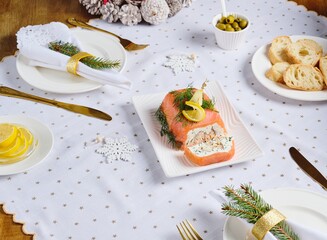 A cold appetizer, a terrine of salted salmon and smoked mackerel with cheese cream and dill, served on a white rectangular plate on a set table.