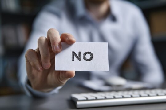 A Close-Up View of a Hand Holding a Card with the Word 'NO' Written on It, Symbolizing Rejection and Disagreement in a Professional Setting