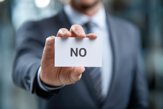 A Businessman in a Suit Displaying a Card with the Word 'NO', Symbolizing Rejection or Denial in a Professional Setting