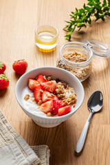 Granola or muesli with natural greek yogurt, strawberry and honey in a bowl on a wooden background