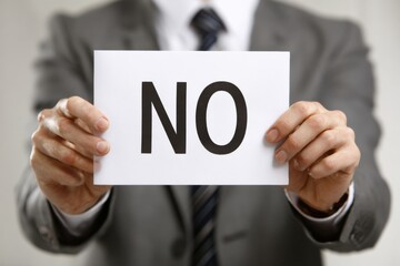 Obraz premium A Professional in a Suit Holding a Sign that Clearly States 'NO', Illustrating Defiance or Rejection in a Formal Business Context