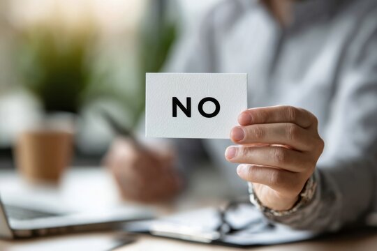 A Defiant Gesture: A Person Holding a Card with 'NO' in Bold Letters, Signifying Rejection or Refusal in a Modern Workspace Setting