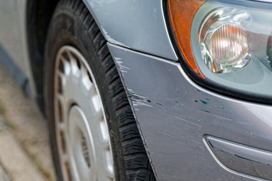 Gray car front side with deep scratch beneath headlight
