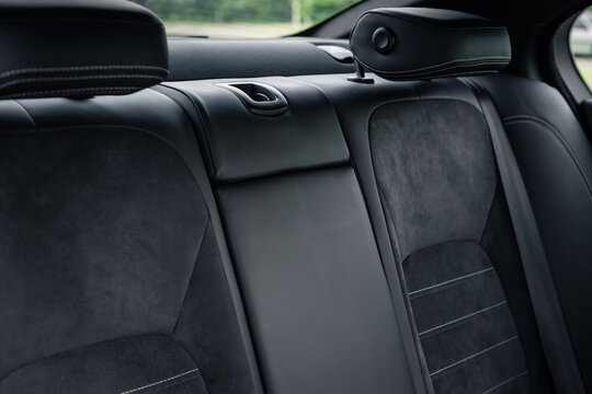 Rear leather seat with cloth inserts in a car. Sedan interior with black leather and cloth seats, green forest in the background.
