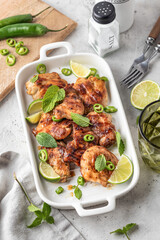Spicy grilled chicken thighs roasted with chilli and lime on white dish, light gray kitchen background