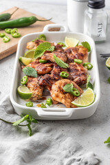 Spicy grilled chicken thighs roasted with chilli and lime on white dish, light gray kitchen background