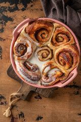 Freshly baked cinnabon buns in a ceramic baking dish on wooden textured background. Top view