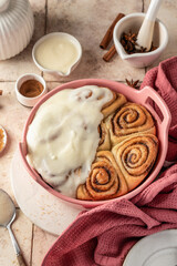Freshly baked glazed cinnabon buns in ceramic baking dish, beige tile background. Making cinnamon rolls process