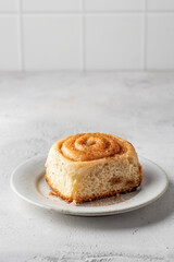 Freshly baked cinnabon bun on ceramic plate on light gray background isolated, copy space. Menu, autumn food concept