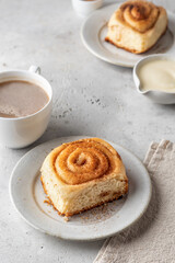 Freshly baked cinnabon bun on ceramic plate and coffee for breakfast on light gray background. Menu, autumn food concept