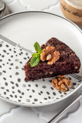 Chocolate spongy brownie cake served with walnuts and mint leaves on top and coffee close up. A piece of chocolate brownie cake