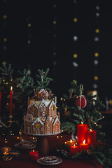 Elegant beautiful Christmas house decoration, stylish holiday decor. Homemade delicious sweet gingerbread house as centrepiece for family dinner. Fir tree branches, candles, stars, garlands