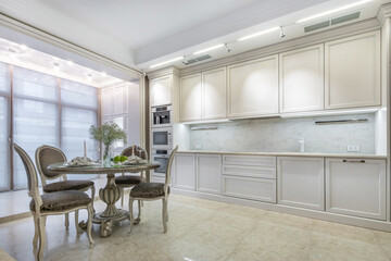 A spacious and stylish kitchen with a glass dining table for four with exquisite dishes in a modern apartment.