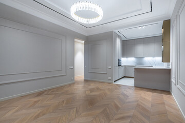 The spacious living room with a beautiful parquet floor and an elegant chandelier seamlessly merges into the kitchen area.