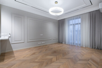 The elegant design of the spacious living room features stylish parquet floors, an elegant chandelier and a large window with beautiful curtains.