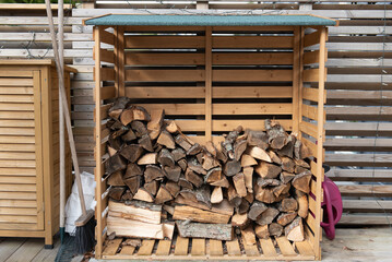 Wooden firewood storage near the house, next to it are garden tools.