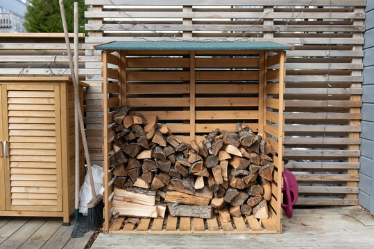 Wooden firewood storage near the house, next to it are garden tools. - Powered by Adobe