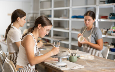 Young woman teacher and girl students sculpt and paint ceramics in workshop
