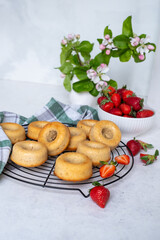 Freshly baked donuts cooling on a wire rack, surrounded by vibrant strawberries and a bouquet of flowers, showcasing delightful pastries in a cozy kitchen setting
