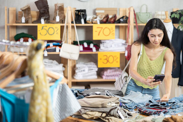 Armenian woman stands near a clothing counter in a store and carefully scans the tags on pants using a barcode. Purchase and payment of clothes by QR code