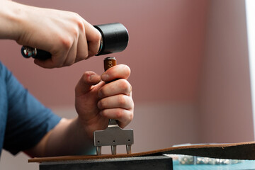 Punching and detailing leather belt holes. Artisan punching holes into a leather strap for a handmade belt on a green cutting mat. Crafting belt holes with punch tool on leather strap.