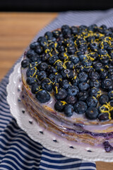 Layered dessert featuring fresh blueberries and lemon zest on top, presented on a decorative white plate with a striped fabric backdrop, showcasing culinary artistry and vibrant colors