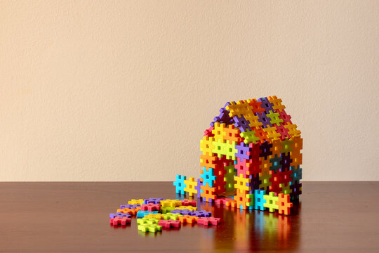 Colorful puzzle house falling apart on wooden table - Powered by Adobe