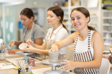 Young woman teacher and two girls students sculpt from clay and paint pottery