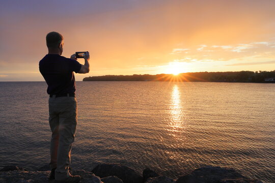 Middle-aged man taking a picture from his cell phone of the sun rising over the water